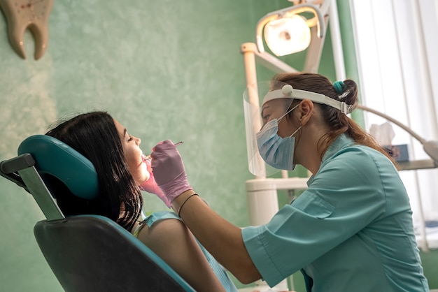 Professioneller Zahnarzt mit Werkzeugen und in Schutzuniform, der den Zahn des Patienten behandelt