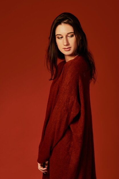 Professionelles Foto einer süßen jungen brünetten Frau in einem schönen roten Boho-Sommerkleid, die in einem Studio auf rotem Hintergrund posiert. Modefrühlingssommerfoto