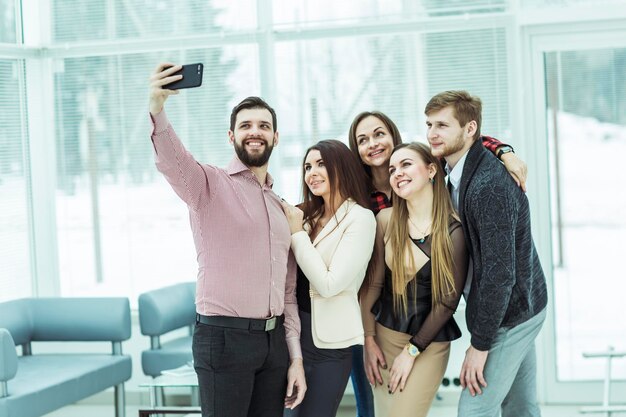 Professionelles Geschäftsteam macht Selfie, während es in der Nähe des Fensters im Büro steht