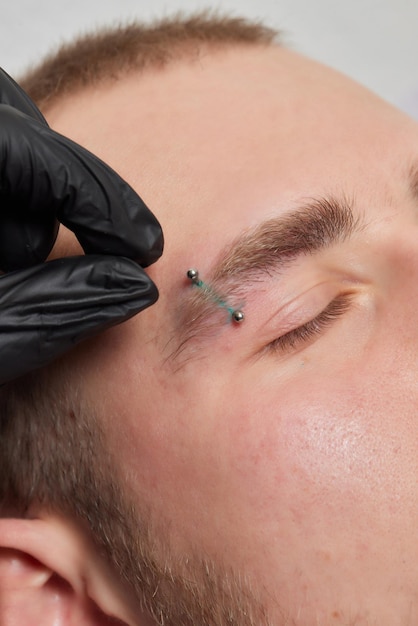 Professionelles Platzieren des Juwels des Piercings auf der Schläfe auf dem Kopf mit Kugeltragus-Typ