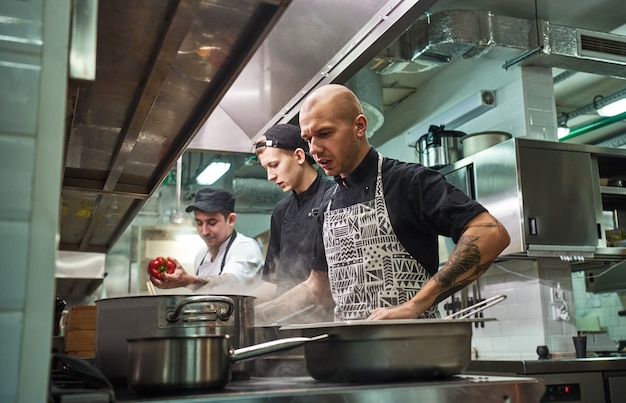 professionelles Team aus Küchenchef und zwei jungen Assistenten, die in einer Restaurantküche kochen