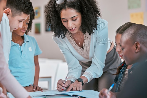 Professor africano ensinando crianças ajudando alunos em sala de aula com lição de casa e escrevendo em livro Diversidade em educação educador lendo caderno infantil e aprendendo em grupo juntos para avaliação