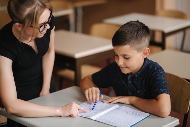 Professor ajudando crianças da escola escrevendo teste na educação em sala de aula, aprendizagem da escola primária e