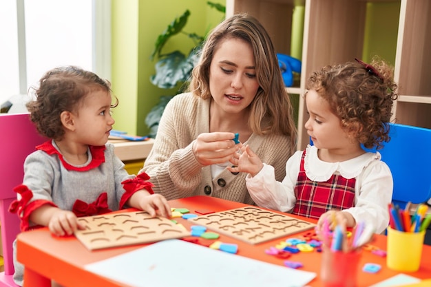 Professor com meninas brincando com jogo de quebra-cabeça de matemática sentado na mesa no jardim de infância