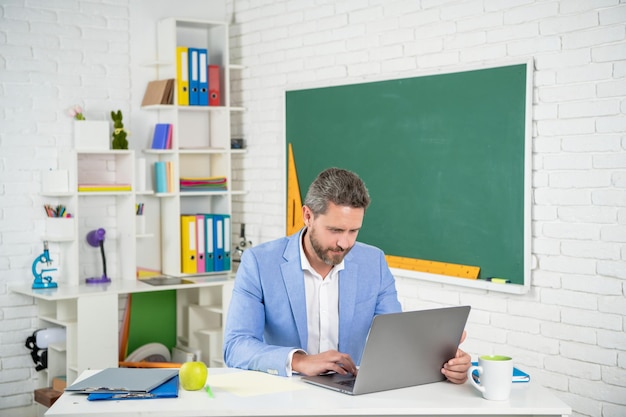 Foto professor de escola alegre em sala de aula com computador no quadro-negro