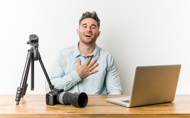 Professor de fotografia bonito jovem ri alto, mantendo a mão no peito.