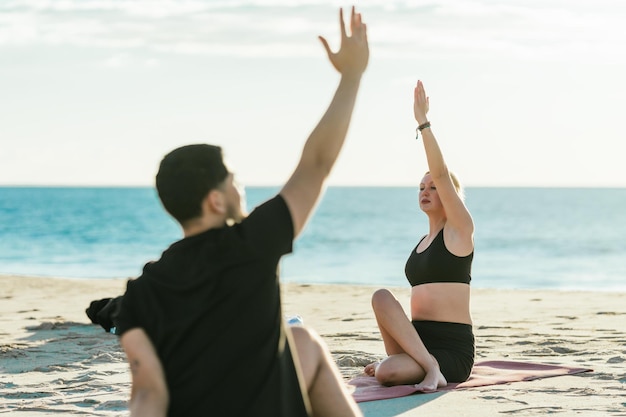 Professor de ioga mostrando uma posição de frente para um homem que faz ioga em uma praia