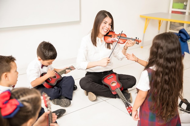 Professor de música mostrando aos alunos como tocar violino em uma sala de aula pré-escolar