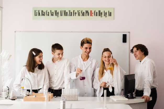 Professor de química da escola mostra frascos de crianças com líquidos para experimentos no laboratório Conceito de educação Aula em grupo de colegas na aula de química