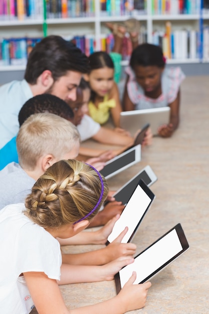 Professor e crianças, deitado no chão, usando tablet digital na biblioteca