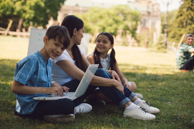 Professor e dois jovens estudantes usam laptop no parque