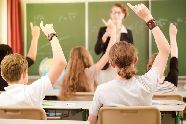 Professor em pé durante a aula em frente a um quadro negro e educa os alunos, que notificam e aprendem em uma aula