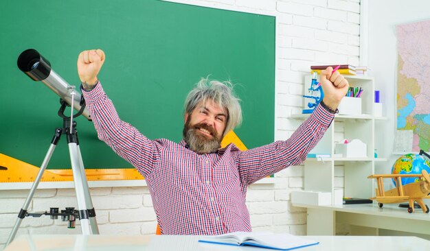 Foto professor entusiasmado no local de trabalho, dia dos professores, professor barbudo feliz à mesa, na sala de aula, a aprender e