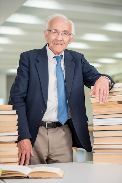 Professor idoso com livros dentro da sala da biblioteca da faculdade