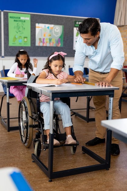 Foto professor masculino biracial feliz com uma menina em cadeira de rodas na aula da escola primária