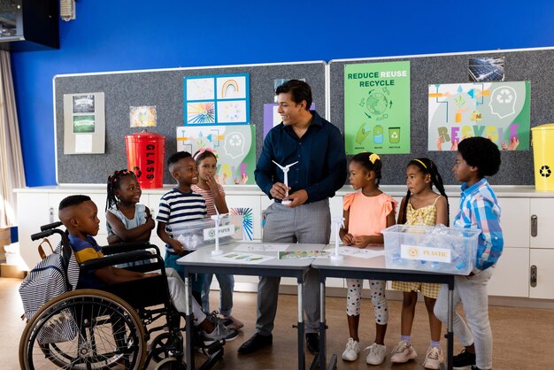 Foto professor masculino feliz e diversificado e crianças com itens de ecologia na aula na escola primária