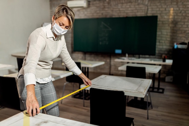 Foto professor medindo o espaço entre as mesas enquanto prepara a sala de aula para o retorno das crianças em idade escolar