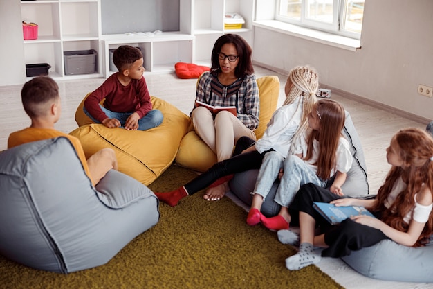 Foto professor sentado em um pufe lendo para os alunos