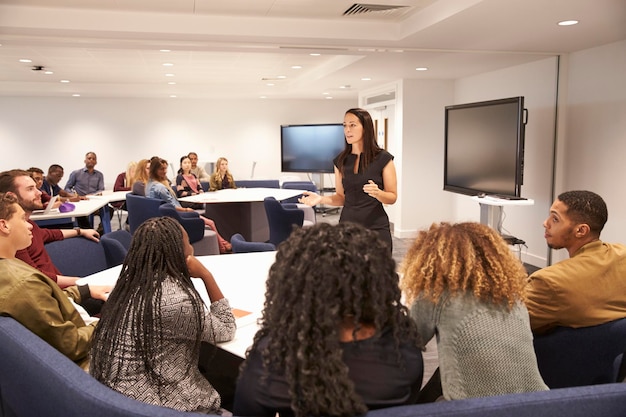 Foto professora abordando estudantes universitários em uma sala de aula