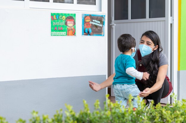 Professora abraçando uma criança de volta à escola usando máscara após a pandemia de coronavírus