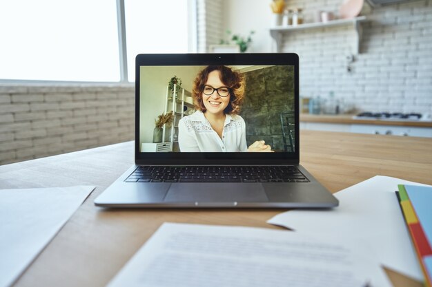 Professora atraente sorrindo para a câmera durante uma videochamada, tendo uma aula online com os alunos