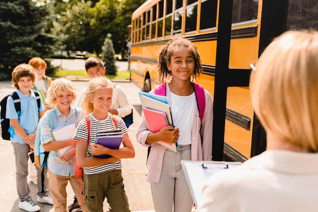 Professora contando grupo de crianças alunos escolares antes de embarcar no ônibus escolar antes das aulas Bem-vindo de volta à escola após as férias de verão Novo semestre do ano escolar