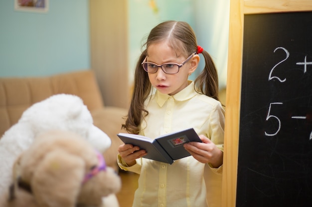 Professora de óculos. Linda garota está ensinando brinquedos em casa na lousa. Educação doméstica pré-escolar.