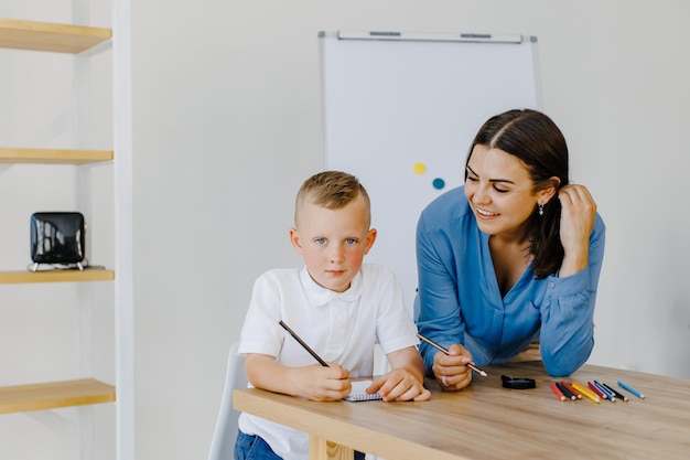 Professora de tutor jovem atenta ajudando o aluno menino a estudar os erros corretos explicando o material de aprendizagem Mãe sorridente ajuda o menino com a tarefa em casa