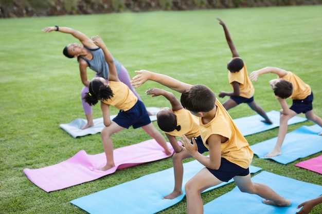 Professora e grupo de diversos alunos realizando exercícios de alongamento no jardim da escola