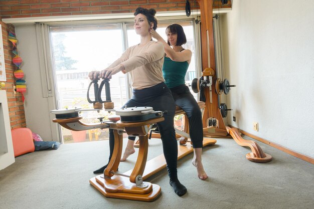 Professora ensinando a sua aluna a técnica correta de exercício em uma máquina de reabilitação para fortalecer e melhorar a saúde das articulações