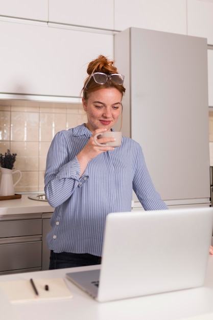 Professora na cozinha com uma xícara de chá durante a aula online