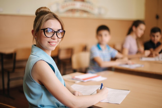 Professora na frente de crianças professora bonita em sala de aula sentada na mesa e perguntando