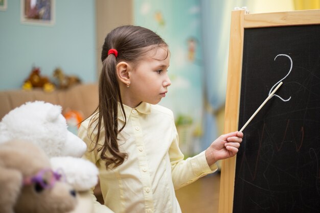 Professorazinha. Linda garota está ensinando brinquedos em casa na lousa. Educação doméstica pré-escolar.