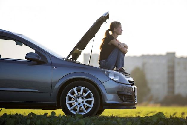 Profil der jungen Frau, die auf Auto mit geknallter Haube sitzt