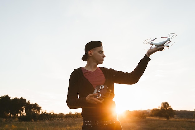 Profil des Mannes, der Drohnen im freien Raum hält Pilot im Freien mit Quadrocopter Sunset Flare auf dem Hintergrund Unterhaltungskonzept für moderne Technologien der Elektronik