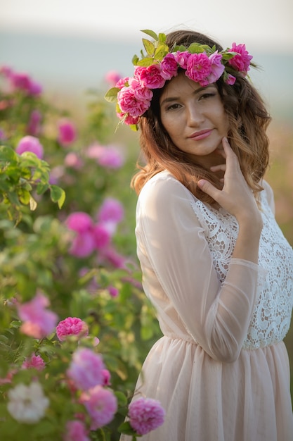 Profil eines Mädchens gegen die von Büschen blühender wilder Rosen mit einem Kranz von Rosen auf ihrem Kopf