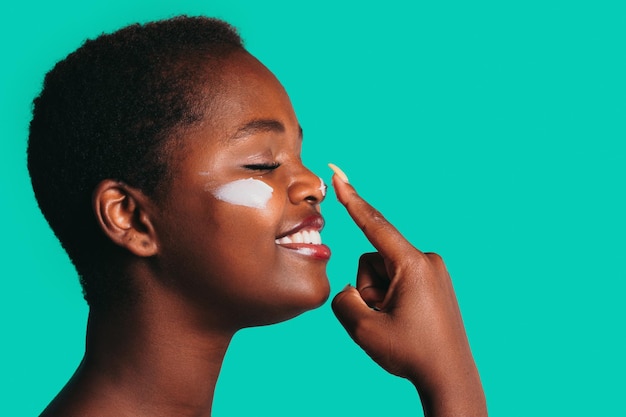 Foto profilansicht einer afrikanischen frau, die die nase mit dem zeigefinger berührt, um die creme aufzutragen, die auf meergrünem hintergrund mit freiem platz für text isoliert ist gesichtsmaske für die schönheitsbehandlung der haut kopieren sie platz