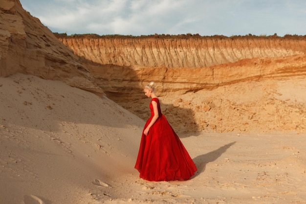 Profilbild in voller Länge einer jungen Frau im roten wehenden Kleid mit fliegendem Stoff auf dem Hintergrund des goldenen Sandes.