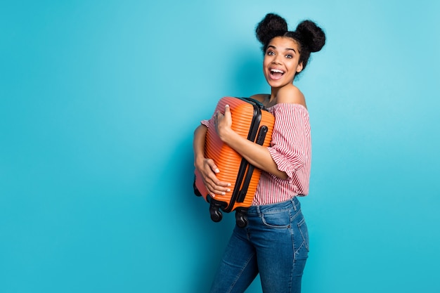 Profilfoto der lustigen hübschen dunklen Haut Dame halten großen schweren Koffer genießen Reisen ins Ausland tragen gestreifte rot weiße schulterfreie Bluse Jeans isoliert blaue Farbe Wand