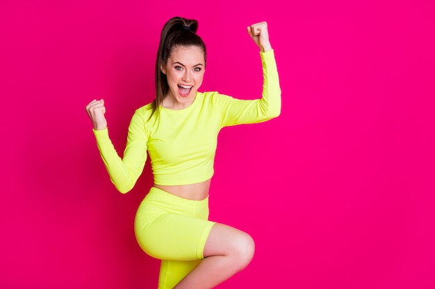 Profilfoto einer erstaunten feiernden entzückenden jungen Dame, die die Fäuste hoch schreit, schreit den Sportanzug einzeln auf leuchtendem rosafarbenem Hintergrund