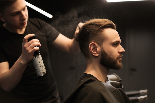 Profilfoto eines jungen Friseurs, der in einem Friseursalon die Haare seiner Kunden mit einem Elektrorasierer und einem Kamm schneidet.