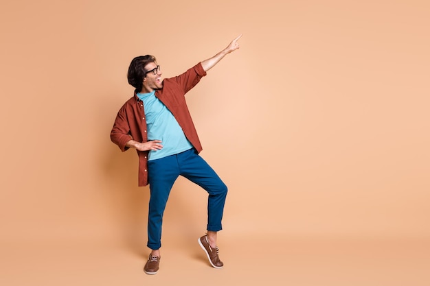 Profilfoto in voller Länge von Guy Dance Direct Finger Up tragen Brille braunes T-Shirt Hosen Schuhe isoliert beigefarbener Hintergrund