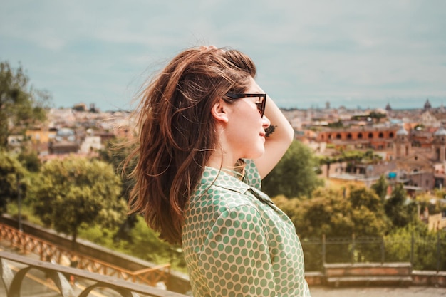 Profilporträt einer jungen lächelnden Frau in Sonnenbrille mit Panoramablick auf Rom, Italien