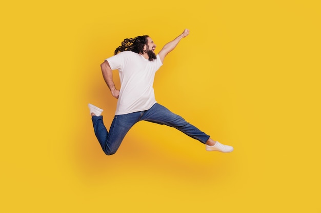 Profilporträt eines inspirierten positiven verrückten Kerls, der schnelle Sprungheldenbewegung auf gelbem Hintergrund läuft