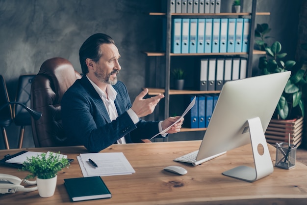 Profilseitenansicht Porträt seines netten gutaussehenden Mannes, qualifizierter Finanzier, der an einem Online-Meeting teilnimmt, in dem es diskutiert wird, Projektstart-Unternehmensrechtdokument moderne Betonindustriearbeitsplatzstation zu diskutieren