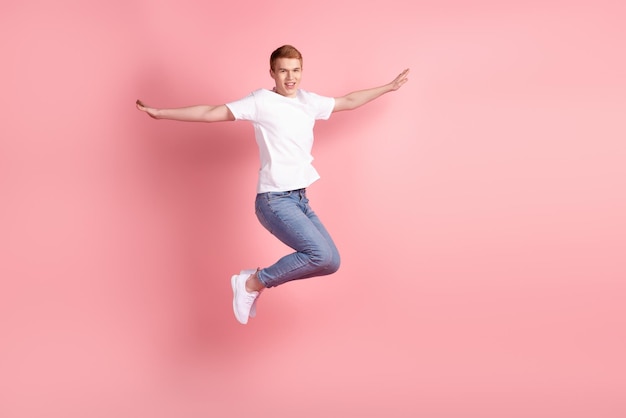 Profilseitenfoto in voller Größe eines jungen, fröhlichen Mannes, der Spaß mit den Händen beim Flügelfliegensprung hat, isoliert über rosafarbenem Hintergrund
