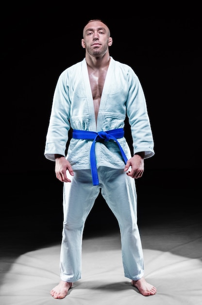 Profisportler steht im Fitnessstudio in einem Kimono mit blauem Gürtel. Konzept von Karate, Jiu-Jitsu, Sambo, Judo. Gemischte Medien