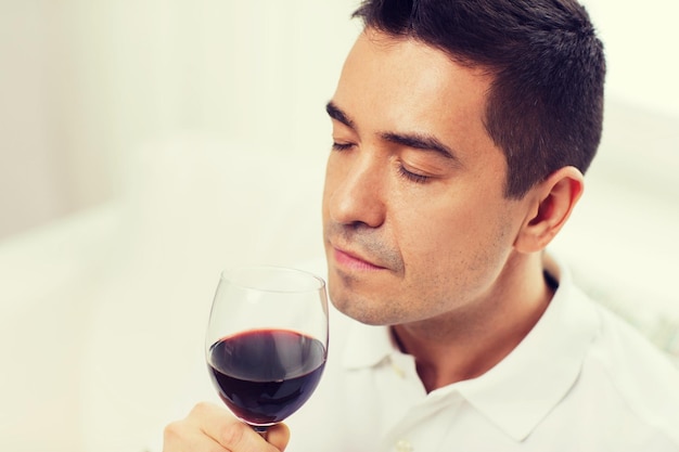 profissão, bebidas, lazer e conceito de pessoas - homem feliz bebendo e cheirando vinho tinto de vidro em casa