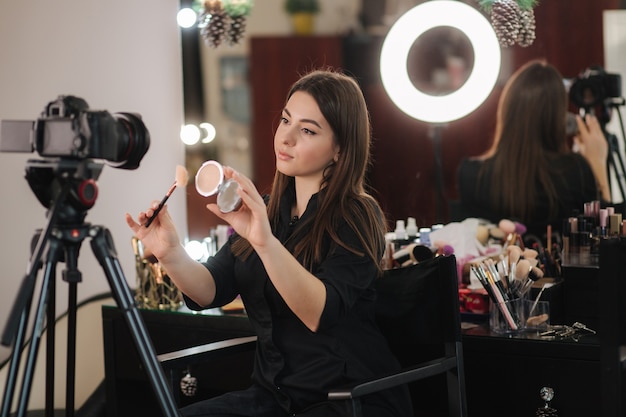 Foto profissão, maquiadora, mulher, resenhando produtos de beleza em um videoblog no estúdio de beleza. mulher