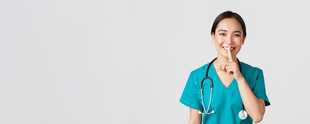 Profissionais de saúde, prevenindo vírus, conceito de campanha de quarentena. médico asiático sorridente, enfermeira de uniforme sorrindo, calando, pedindo para ficar quieto, em pé fundo branco